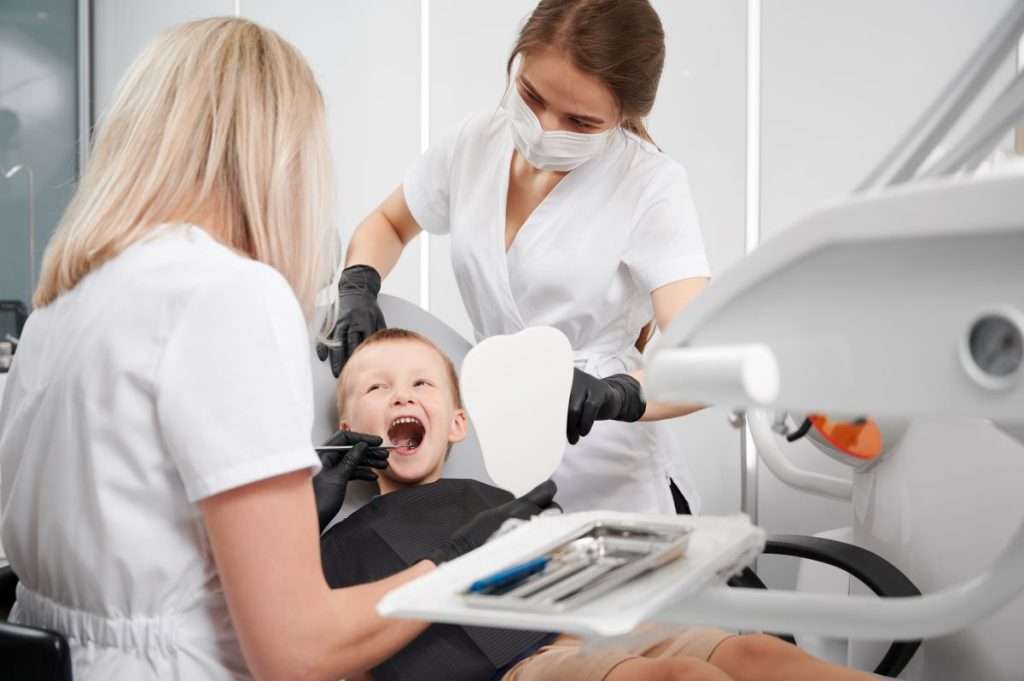 Dentist and assistant using advanced tools for a comfortable pediatric dental exam. Child is smiling. Mississauga Smiles Dentistry.