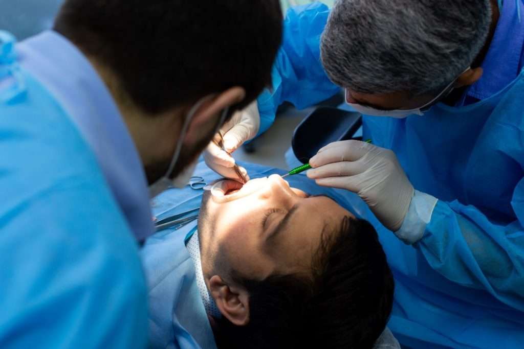 Two dentists performing a wisdom tooth removal procedure using sterile instruments in a safe dental environment.