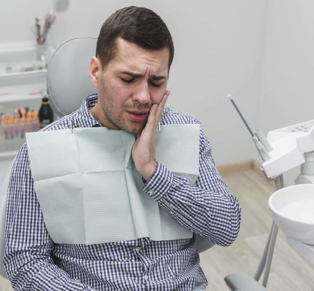Young man holding his cheek in a clinic, experiencing severe facial pain from TMD or Bruxism symptoms. Mississauga Smiles Dentistry, Mississauga.