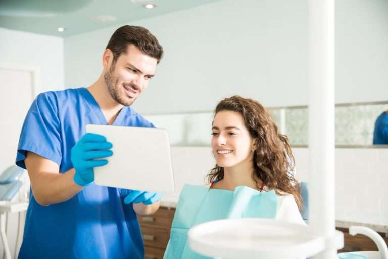 Dentist showing CEREC crown options to a smiling patient on a tablet in a dental clinic