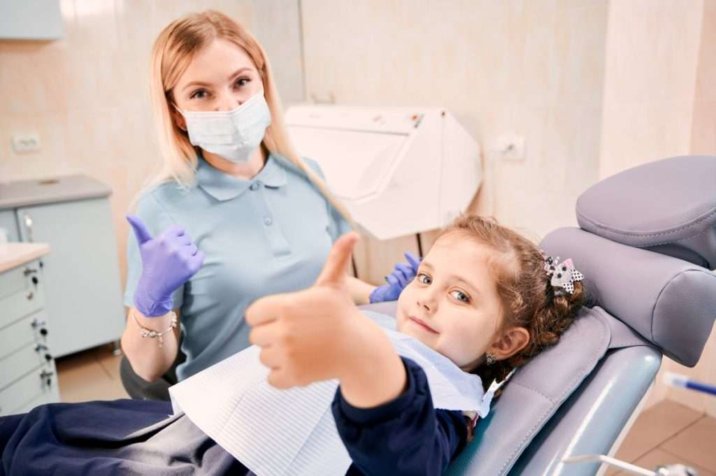 Happy child and dentist giving the "OK" sign after receiving Gentle Dental Care. Pediatric Dentistry at Mississauga Smiles Dentistry.
