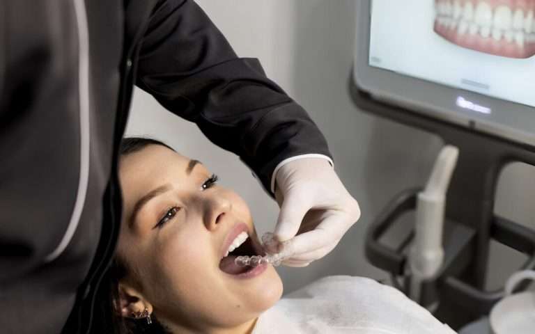 Dentist fitting clear aligners for a patient with 3D dental scan on screen.