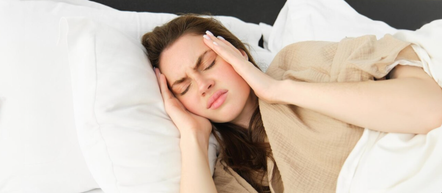 Woman waking up with hand on her head, experiencing sleep apnea symptoms like headache and fatigue.