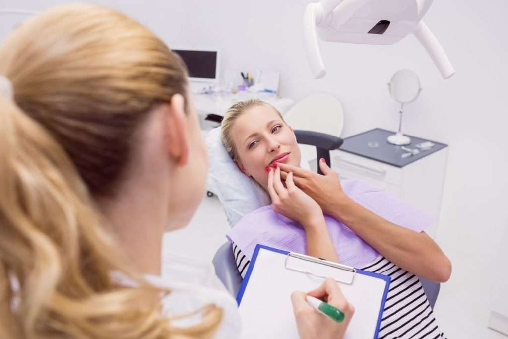 Female patient with cheek pain during dental consultation about wisdom tooth removal symptoms.